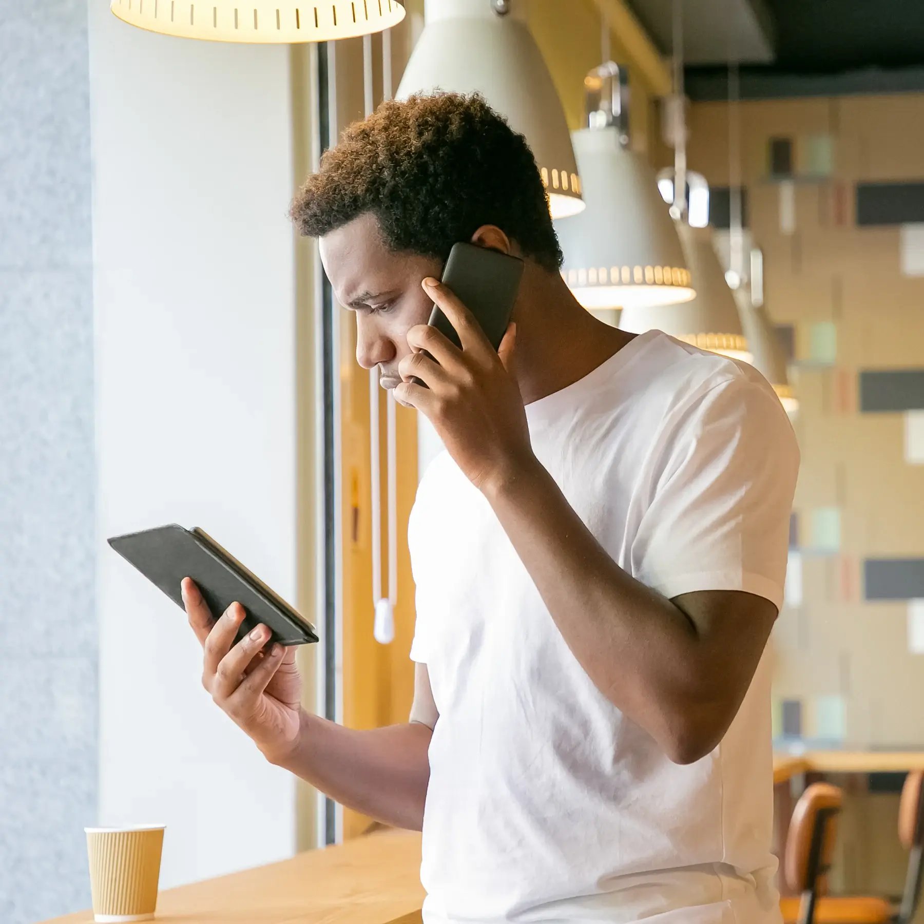 focused-african-american-guy-talking-cell-looking-tablet-screen