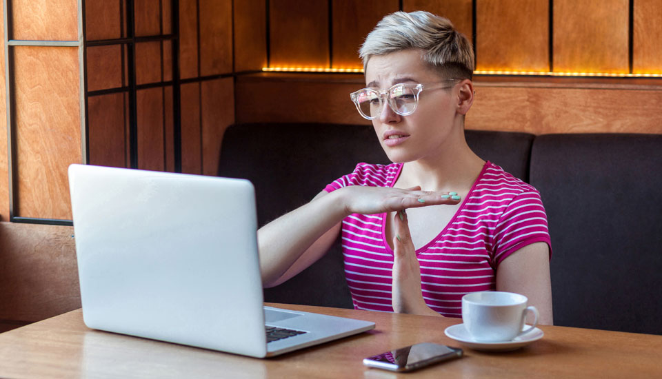 Woman with short blonde hair with laptop holding up a time out sign with her hands to bad credit loan lenders.