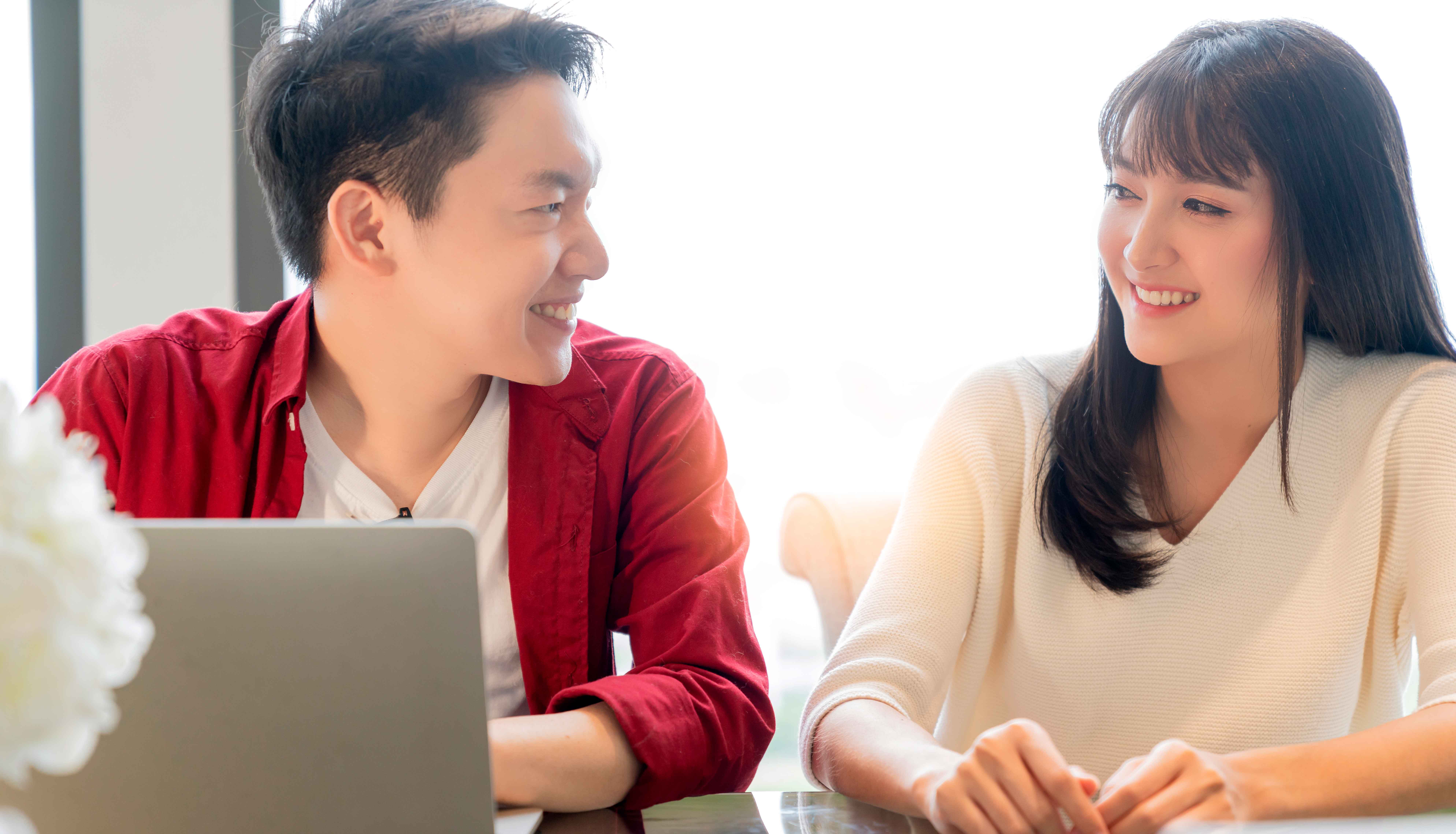 Asian couple discussing unsecured loans at the kitchen table together smiling.